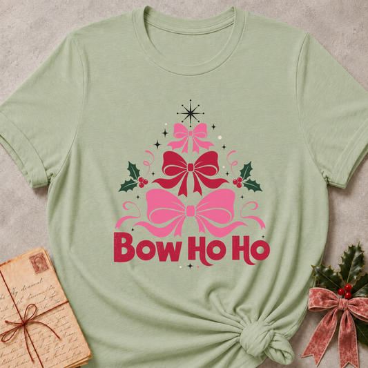 A sage green short-sleeve t-shirt with a 'Bow Ho Ho' Christmas graphic, styled in a flat-lay with a vintage letter and a velvet bow on a neutral textured background.