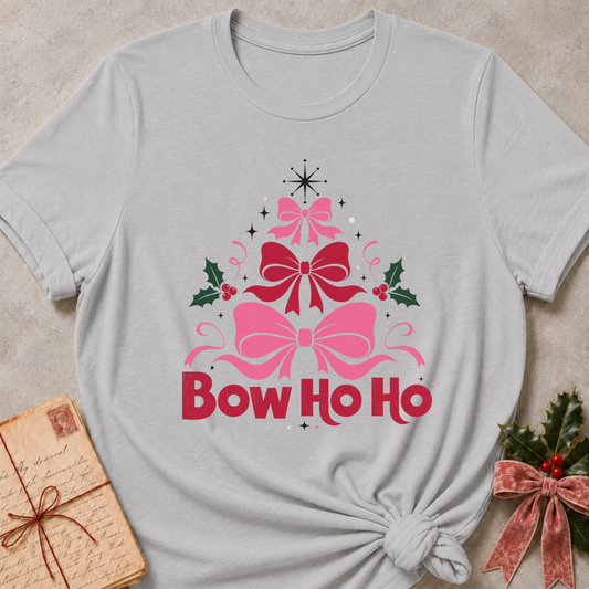 A light gray short-sleeve t-shirt with a 'Bow Ho Ho' Christmas graphic, styled in a flat-lay with a vintage letter and greenery on a textured beige background.