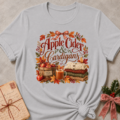 Athletic Heather relaxed fit tee with Apple Cider and Cardigans lettering, a cider mug, a basket of red apples, stacked sweaters and a gingham bow