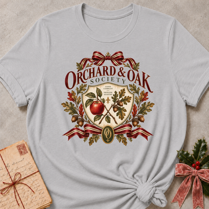 Athletic heather grey women's relaxed tee with a vintage Orchard & Oak Society crest featuring a red apple, oak leaves, acorns, and striped ribbon bows