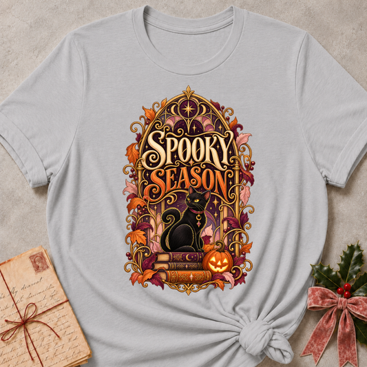 Athletic Heather Spooky Season tee with a black cat on spellbooks beside a glowing jack-o'-lantern under a golden Gothic arch