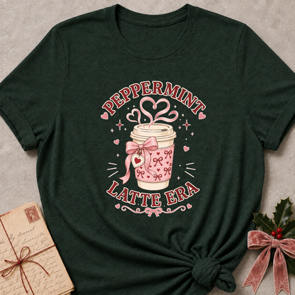 A dark forest green t-shirt with a 'Peppermint Latte Era' graphic print, styled in a flat-lay with a vintage postcard and holly on a gray textured background.