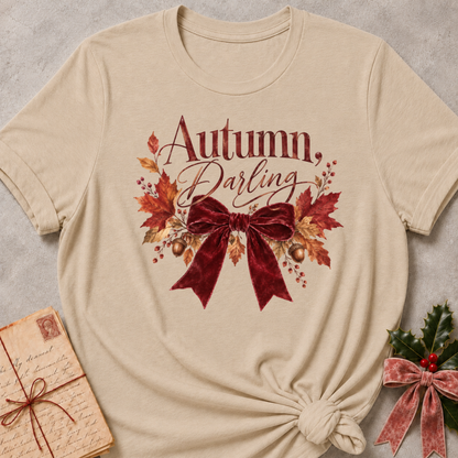 Autumn, Darling script with a burgundy velvet bow, golden acorns, and falling leaves on a warm heather stone relaxed fit tee