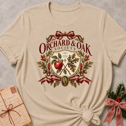 Heather stone women's relaxed tee with a vintage Orchard & Oak Society crest featuring a red apple, oak leaves, acorns, and striped ribbon bows