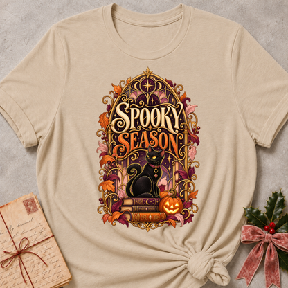 Heather Stone Spooky Season tee with a black cat on spellbooks beside a glowing jack-o'-lantern under a golden Gothic arch