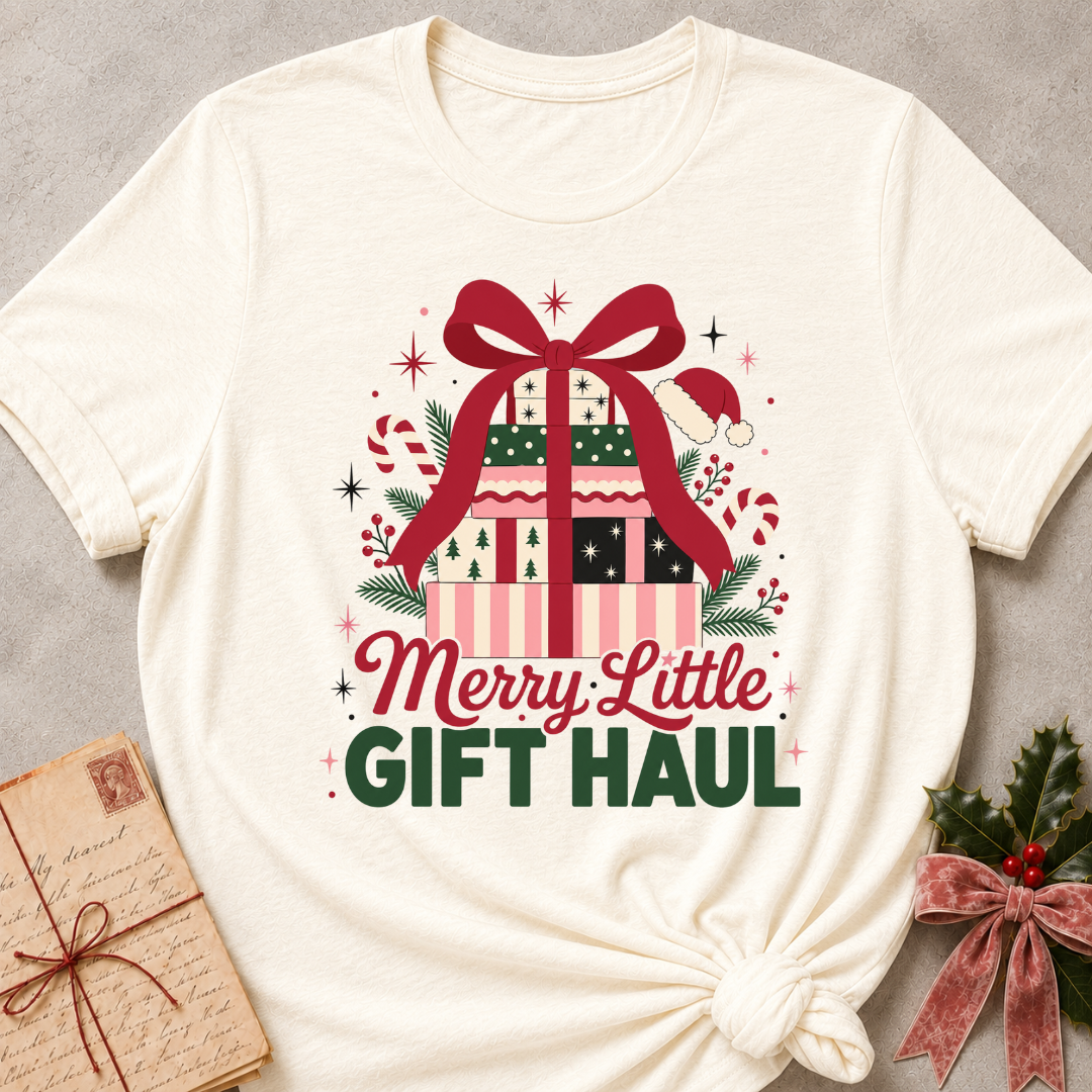 An off-white graphic t-shirt featuring a festive Christmas gift illustration with the text 'Merry Little GIFT HAUL'. The t-shirt is styled flat on a gray textured background with a vintage postcard and holly in the corners.