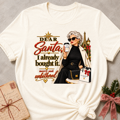 Natural relaxed fit tee with Dear Santa, I already bought it lettering, a merry and unbothered shopper in sunglasses with an iced coffee and gift bags