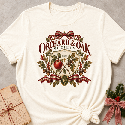 Natural cream women's relaxed tee with a vintage Orchard & Oak Society crest featuring a red apple, oak leaves, acorns, and striped ribbon bows