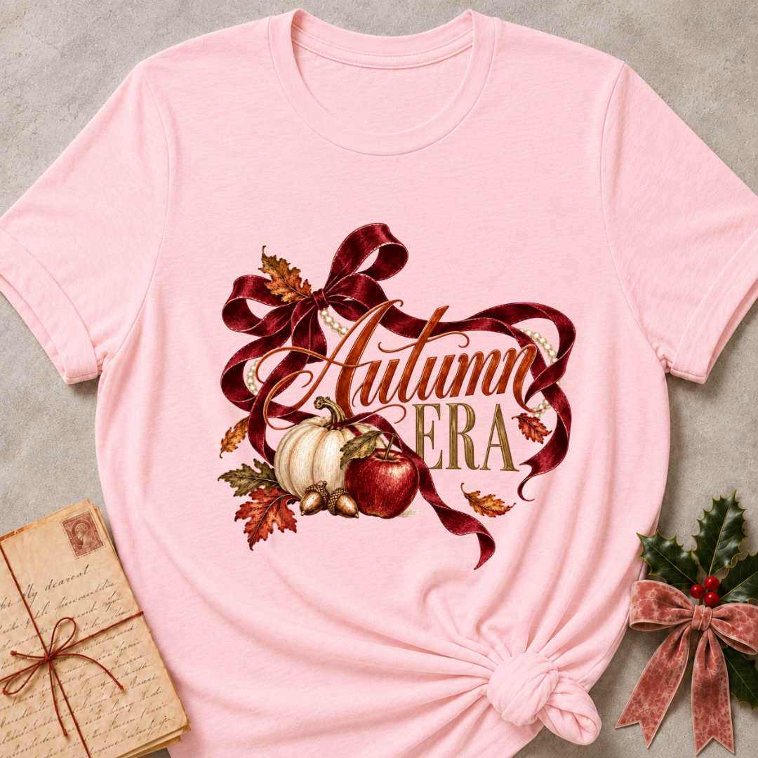 Pink women's relaxed tee with Autumn Era script framed by a burgundy ribbon, pearls, a cream pumpkin, a red apple, and fall leaves
