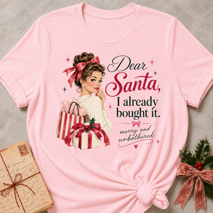 Pink relaxed fit tee with Dear Santa, I already bought it lettering, a vintage holiday shopper with striped gift boxes and red bows