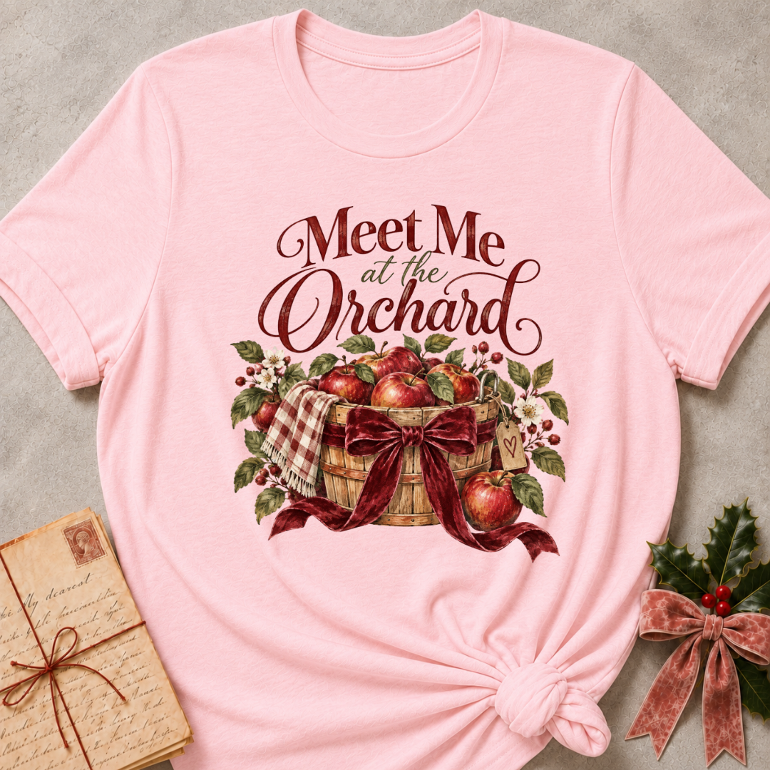 Pink relaxed fit tee with Meet Me at the Orchard lettering, a harvest basket of red apples, blossoms and a burgundy bow