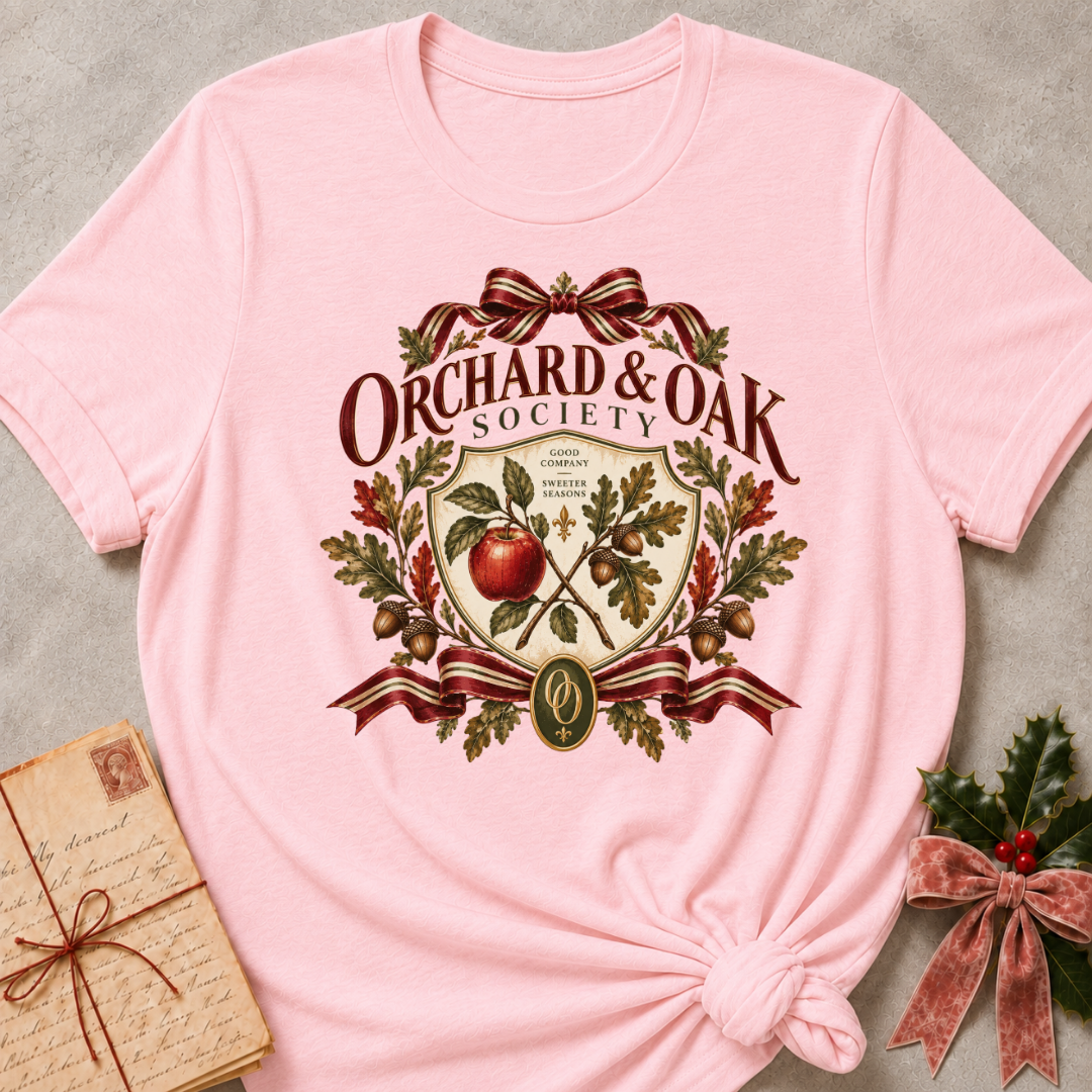 Pink women's relaxed tee with a vintage Orchard & Oak Society crest featuring a red apple, oak leaves, acorns, and striped ribbon bows