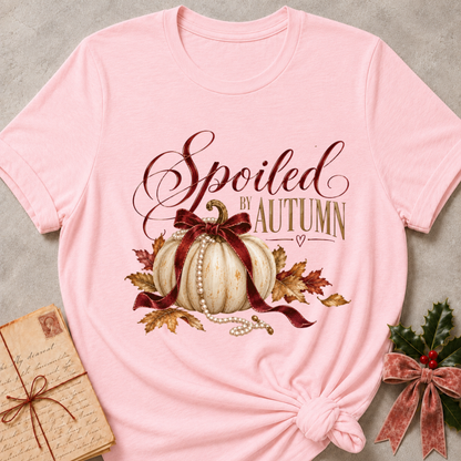 Pink women's relaxed tee with Spoiled by Autumn script over a cream pumpkin tied in a burgundy velvet bow, pearls, and fall leaves