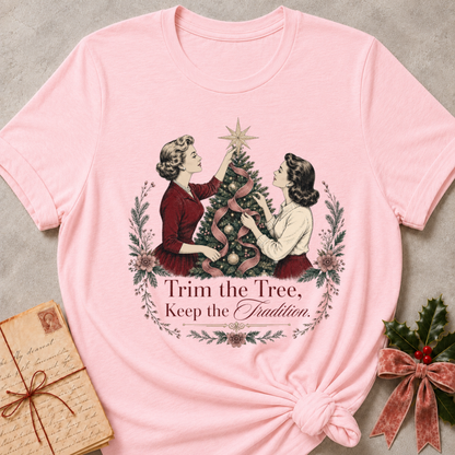 Soft pink relaxed fit tee with two vintage women trimming a Christmas tree and Trim the Tree Keep the Tradition lettering