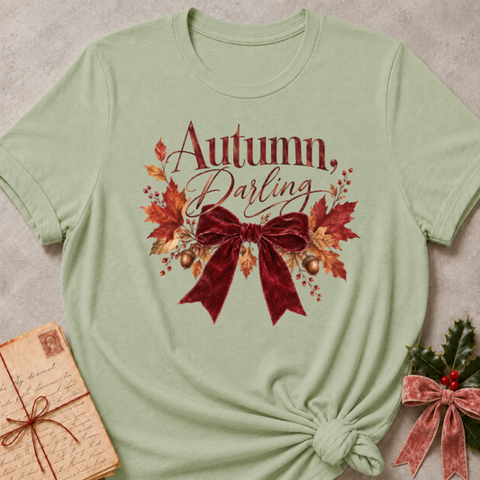 Autumn, Darling script with a burgundy velvet bow, golden acorns, and falling leaves on a soft sage relaxed fit tee