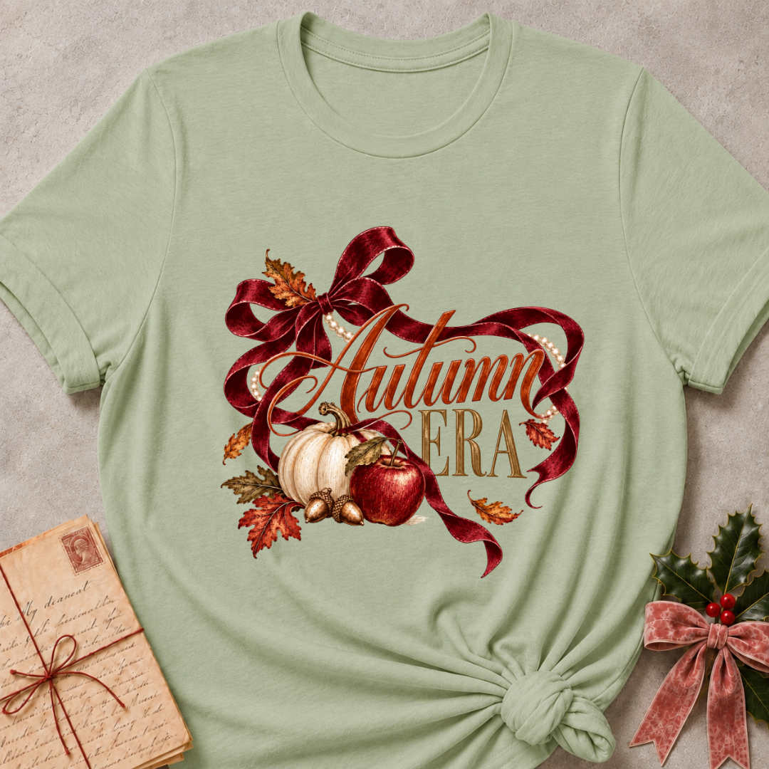 Sage women's relaxed tee with Autumn Era script framed by a burgundy ribbon, pearls, a cream pumpkin, a red apple, and fall leaves