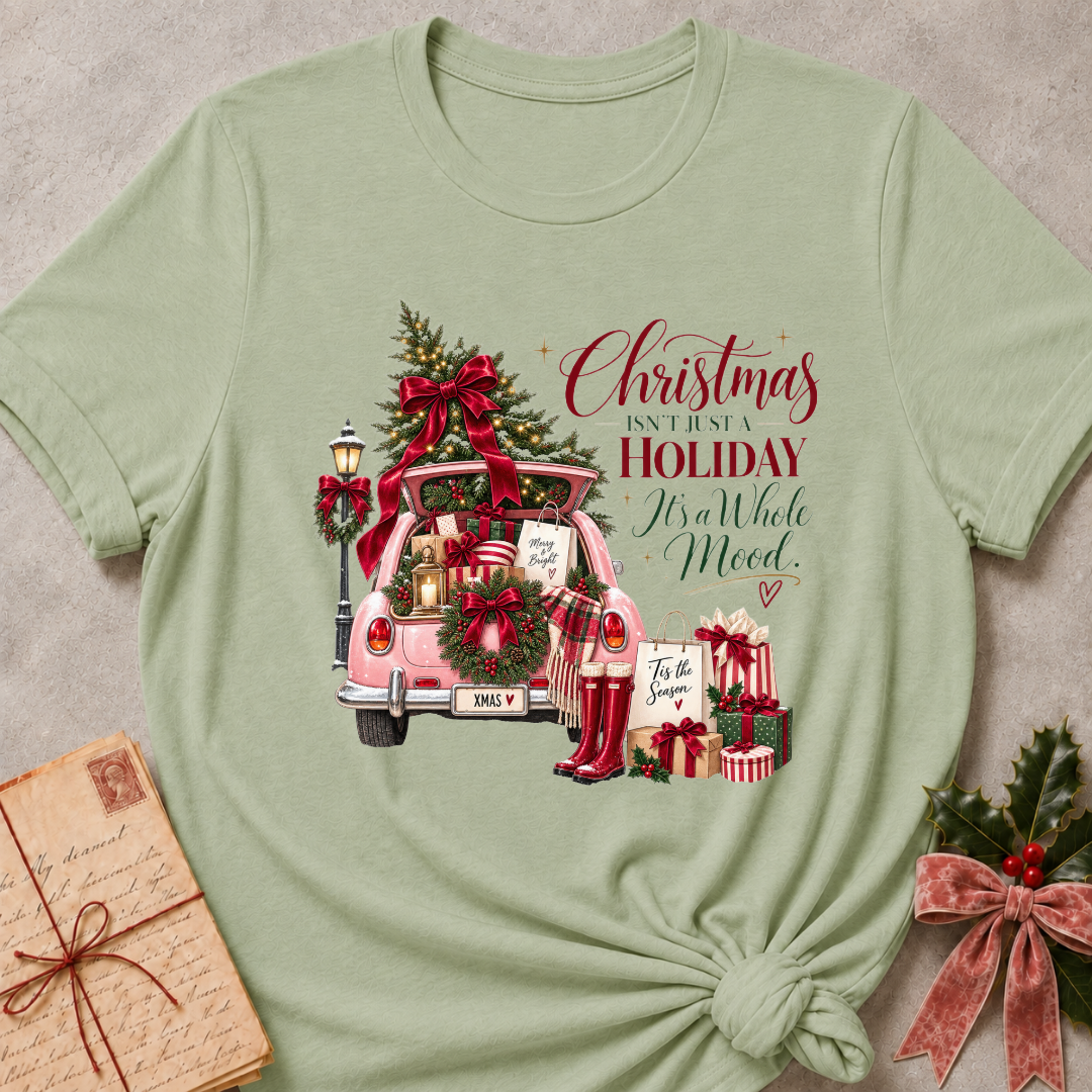 Sage green relaxed fit tee with a pink Christmas truck full of gifts and Christmas Isn't Just A Holiday It's A Whole Mood lettering