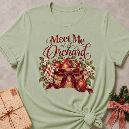 Sage relaxed fit tee with Meet Me at the Orchard lettering, a harvest basket of red apples, blossoms and a burgundy bow