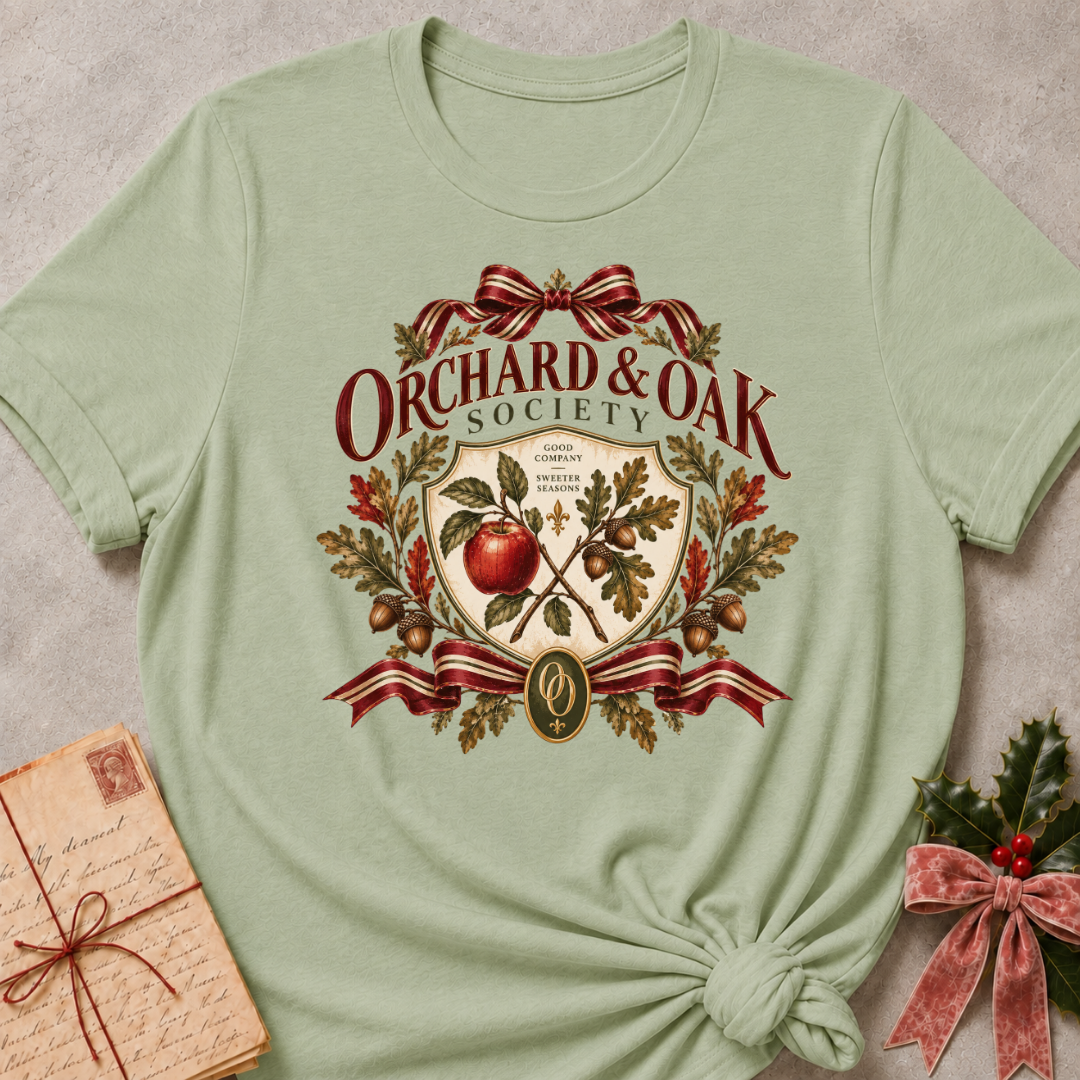 Sage women's relaxed tee with a vintage Orchard & Oak Society crest featuring a red apple, oak leaves, acorns, and striped ribbon bows