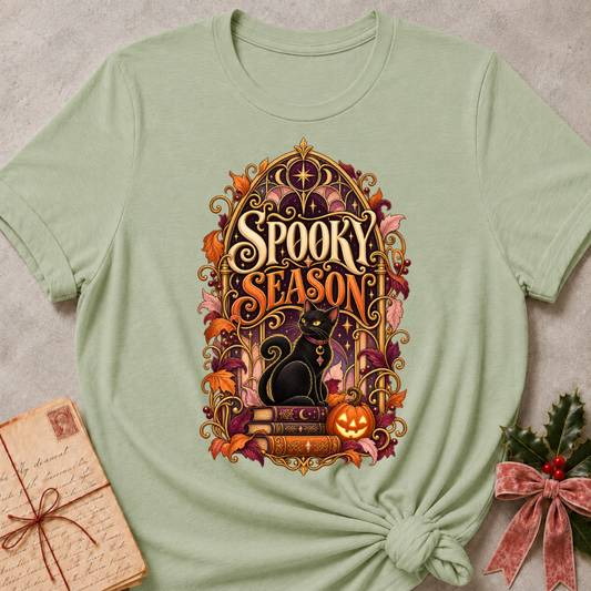 Sage Spooky Season tee with a black cat on spellbooks beside a glowing jack-o'-lantern under a golden Gothic arch