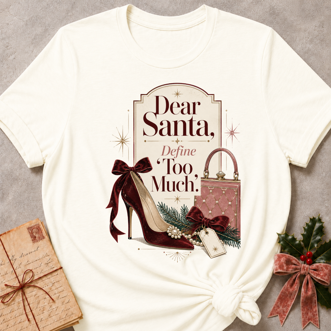 An off-white graphic t-shirt styled in a flat-lay arrangement on a textured gray background, accompanied by a wrapped gift box, a pink patterned purse, a burgundy high heel, and holly with a red bow.