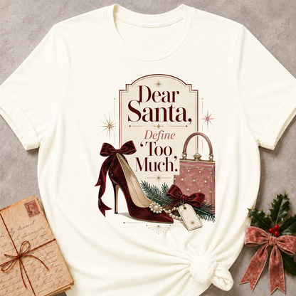 An off-white graphic t-shirt styled in a flat-lay arrangement on a textured gray background, accompanied by a wrapped gift box, a pink patterned purse, a burgundy high heel, and holly with a red bow.