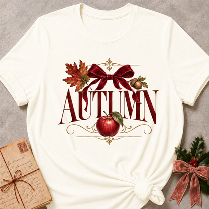 Vintage white women's relaxed tee with a vintage AUTUMN serif design with a burgundy velvet bow, maple leaf, acorn, and red apple