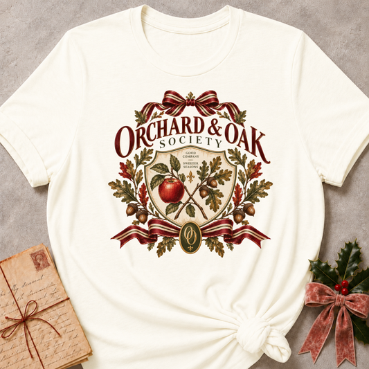 Vintage white women's relaxed tee with a vintage Orchard & Oak Society crest featuring a red apple, oak leaves, acorns, and striped ribbon bows